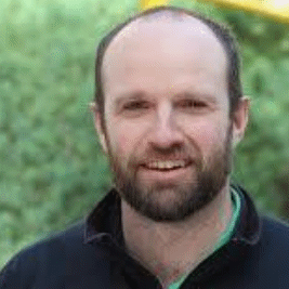 Smiling bearded man outdoors with blurred greenery