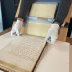 Gloved hands handling historic handwritten manuscript book